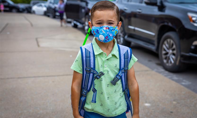 A boy wearing a green shirt and a mask arrives at school